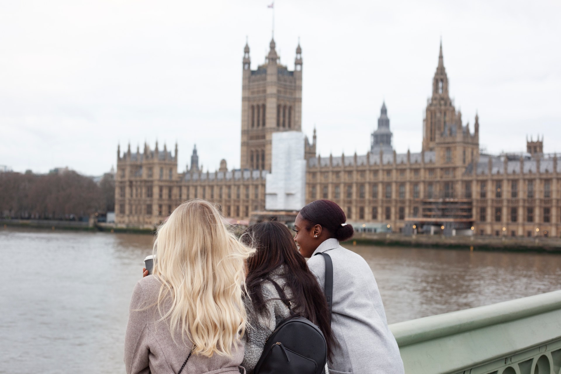 Drei junge Frauen an der Themse in London, hinter ihnen der Westminster-Palast